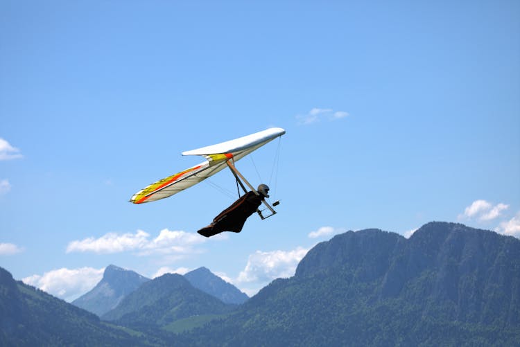 Person Hang Gliding Above Mountains Under Blue Sky