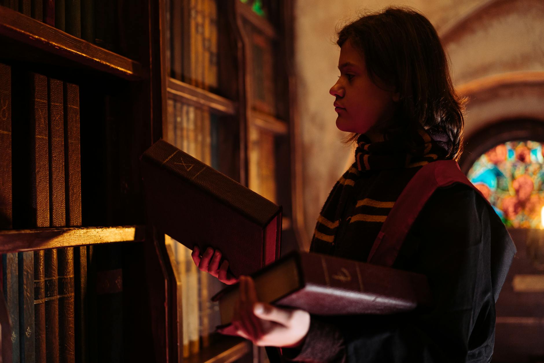 A young wizard in a mystical library holding large books and exploring magic. Fantasy and mystery theme.