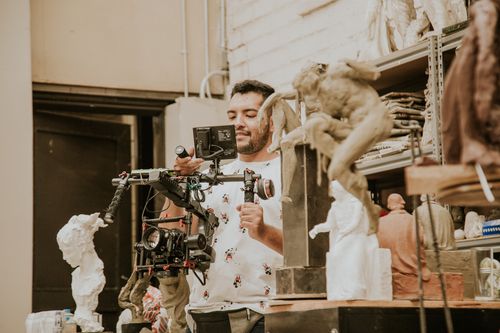 Free A man using a video camera to capture art sculptures in a studio setting. Stock Photo