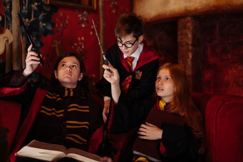 Free Three children in cosplay costumes holding wands and reading books, indoors. Stock Photo