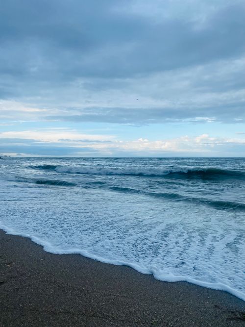 Free Peaceful coastal scene with gentle waves and cloudy sky, perfect for relaxation themes. Stock Photo