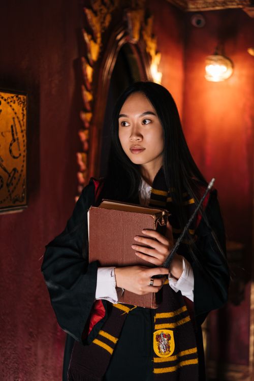 Free An Asian woman dressed in a fantasy sorceress costume, holding a book and magic wand. Stock Photo
