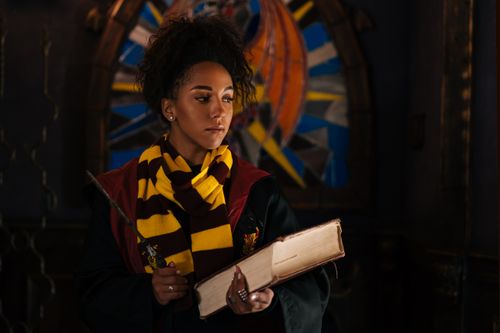 Free Young black woman in wizard cosplay holding a wand and book indoors. Stock Photo