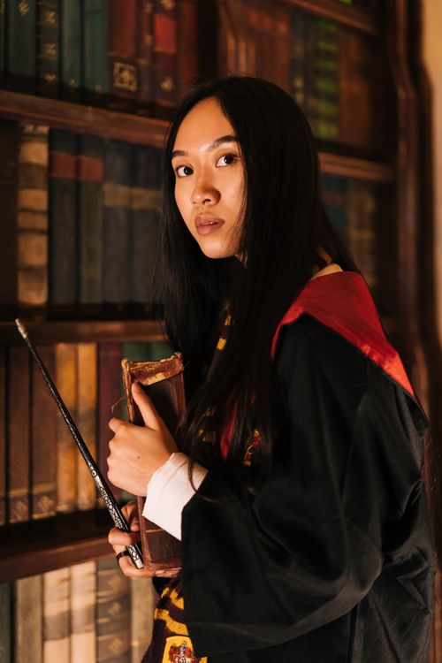 Free A woman dressed in a fantasy wizard costume holds a wand and a book in a library. Stock Photo