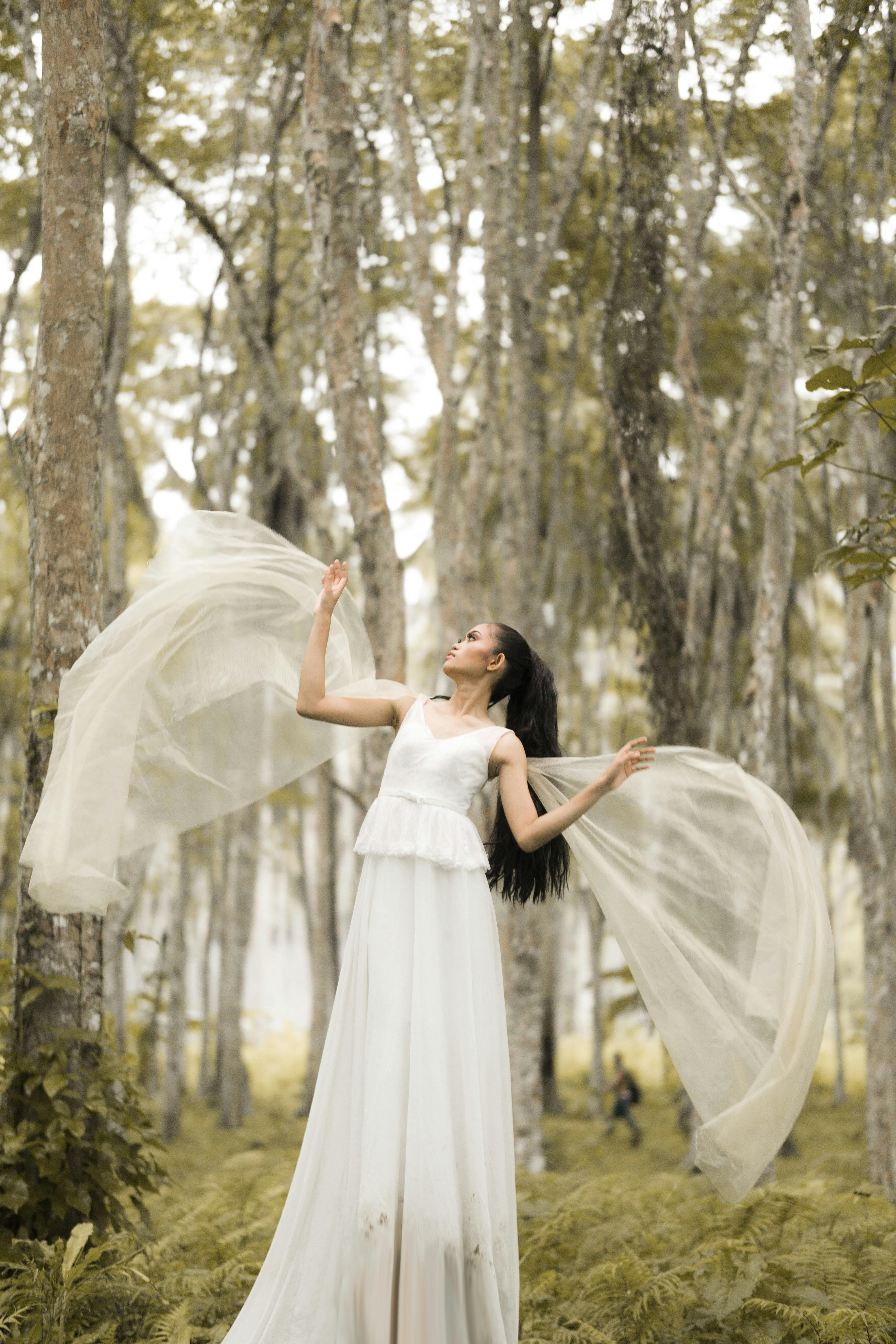 Woman in flowing white dress in serene forest, exuding elegance and grace.