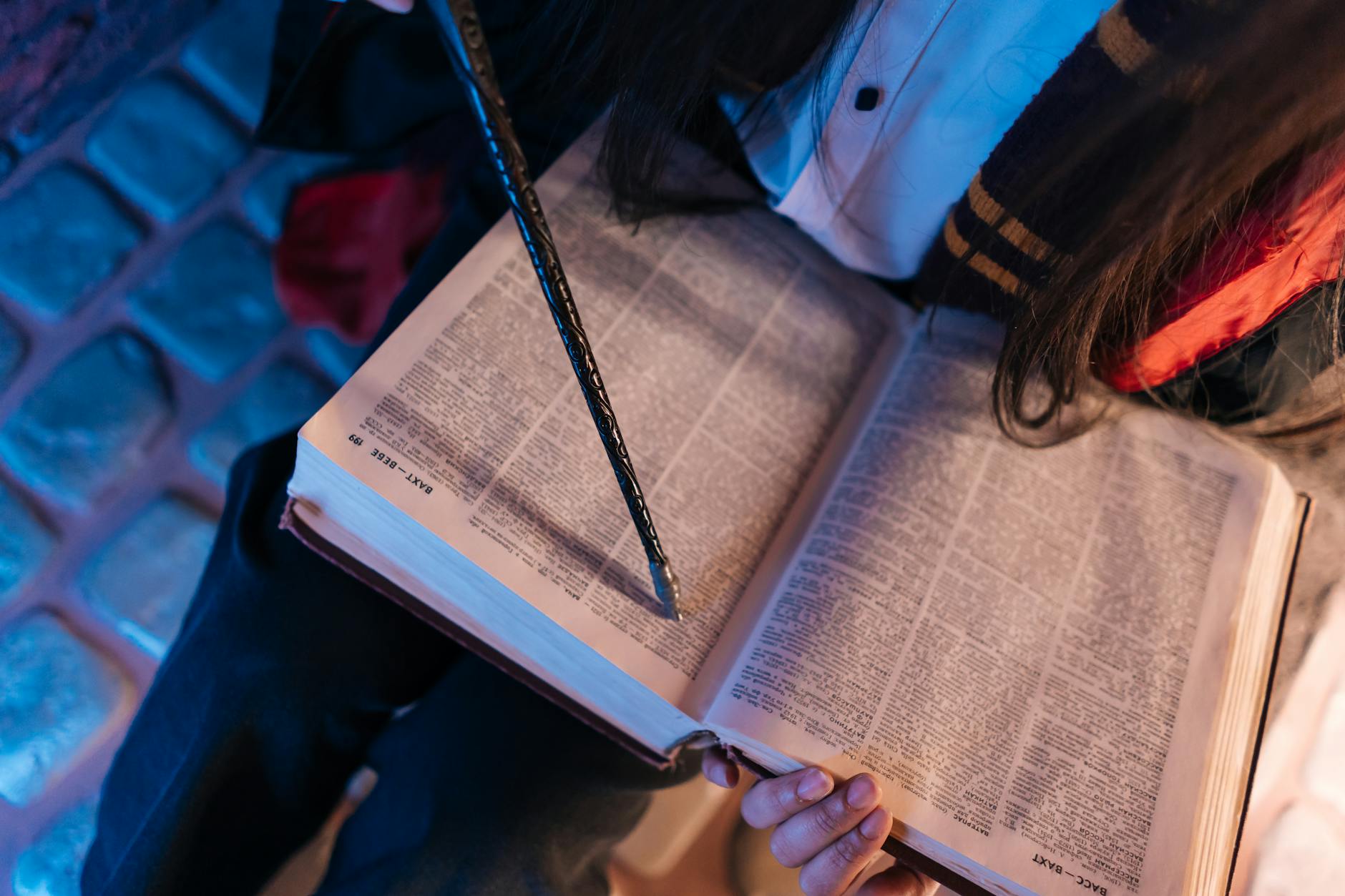 A person holding an open book and wand, capturing a magical and cozy reading atmosphere.