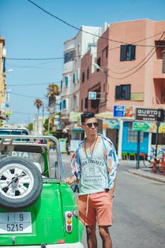 Fashionable man poses by green car in sunny Essaouira street scene, Morocco.