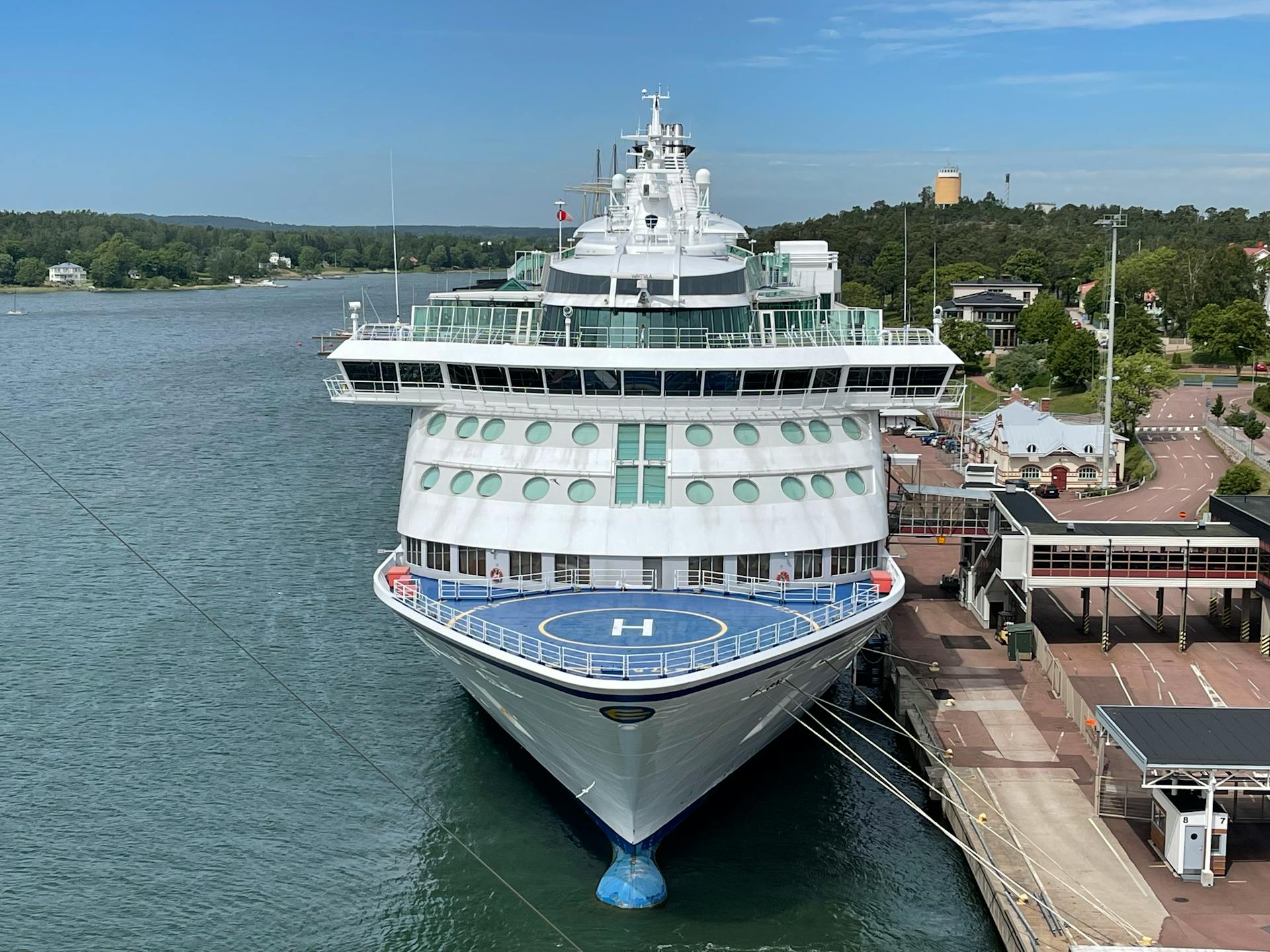 Luxury cruise ship docked at a port surrounded by lush greenery under a clear blue sky.