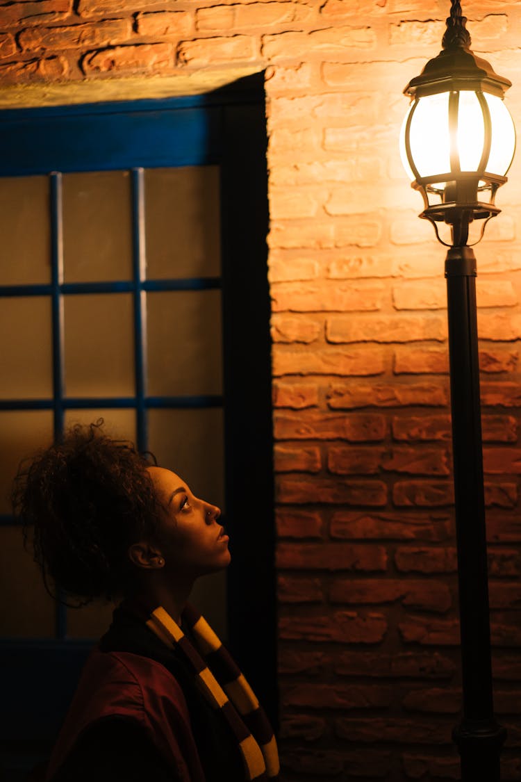 Woman Standing In Black Robe Looking Up On A Light Post