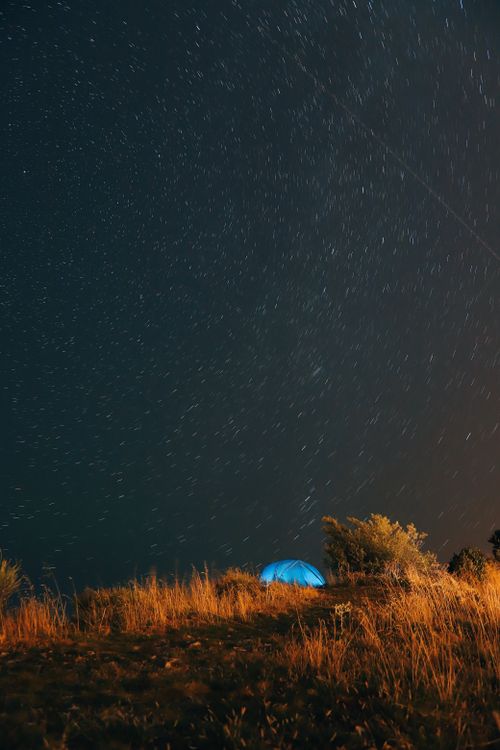 Free A tent set under a starry night sky on a hill, perfect for astronomy and camping enthusiasts. Stock Photo