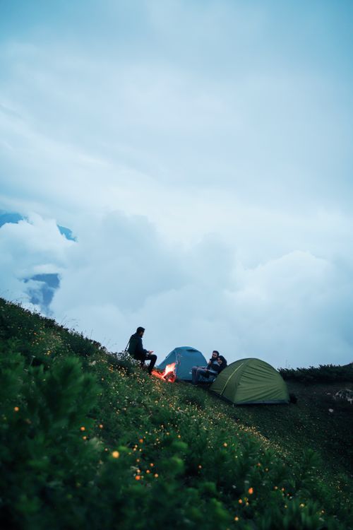 Free Camping on a mountainside with a campfire and tents beneath a cloudy sky, evoking a sense of adventure. Stock Photo