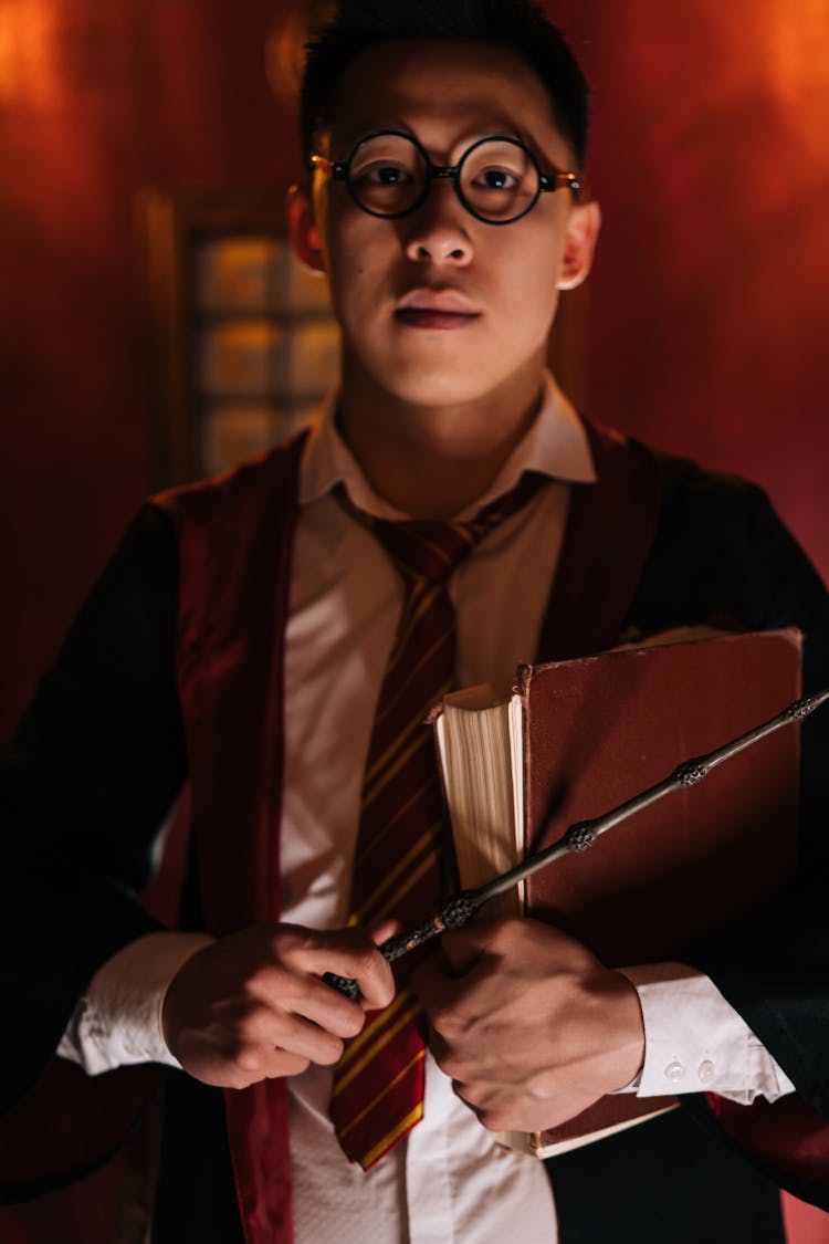 A Man Wearing Eyeglasses Holding Wand And Book