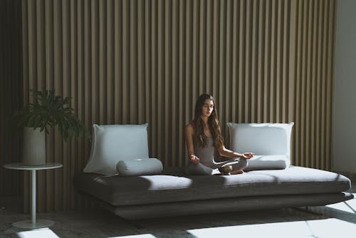 Free A Woman Sitting on the Couch while Meditating with Her Eyes Closed Stock Photo