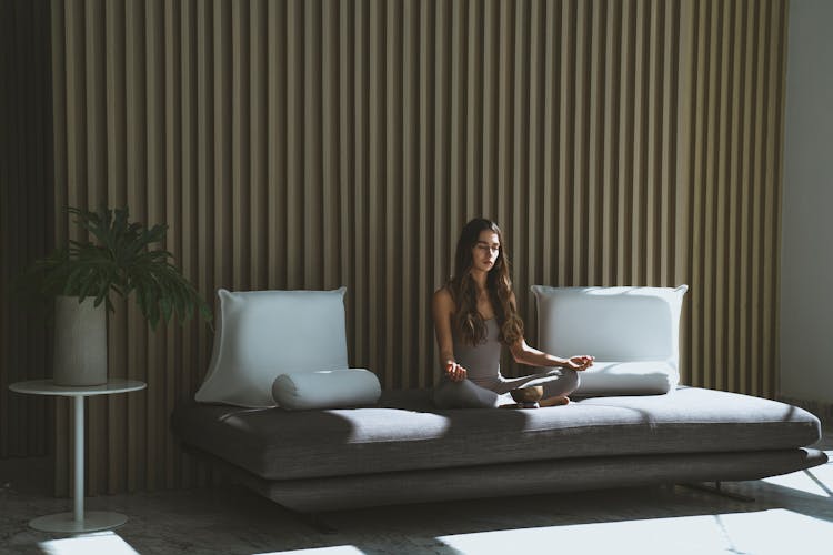 A Woman Sitting On The Couch While Meditating With Her Eyes Closed