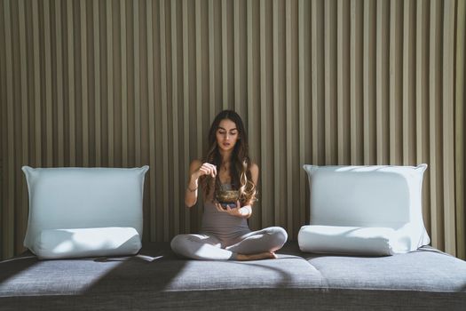 Woman sitting cross-legged on a sofa meditating with incense in a serene indoor setting.