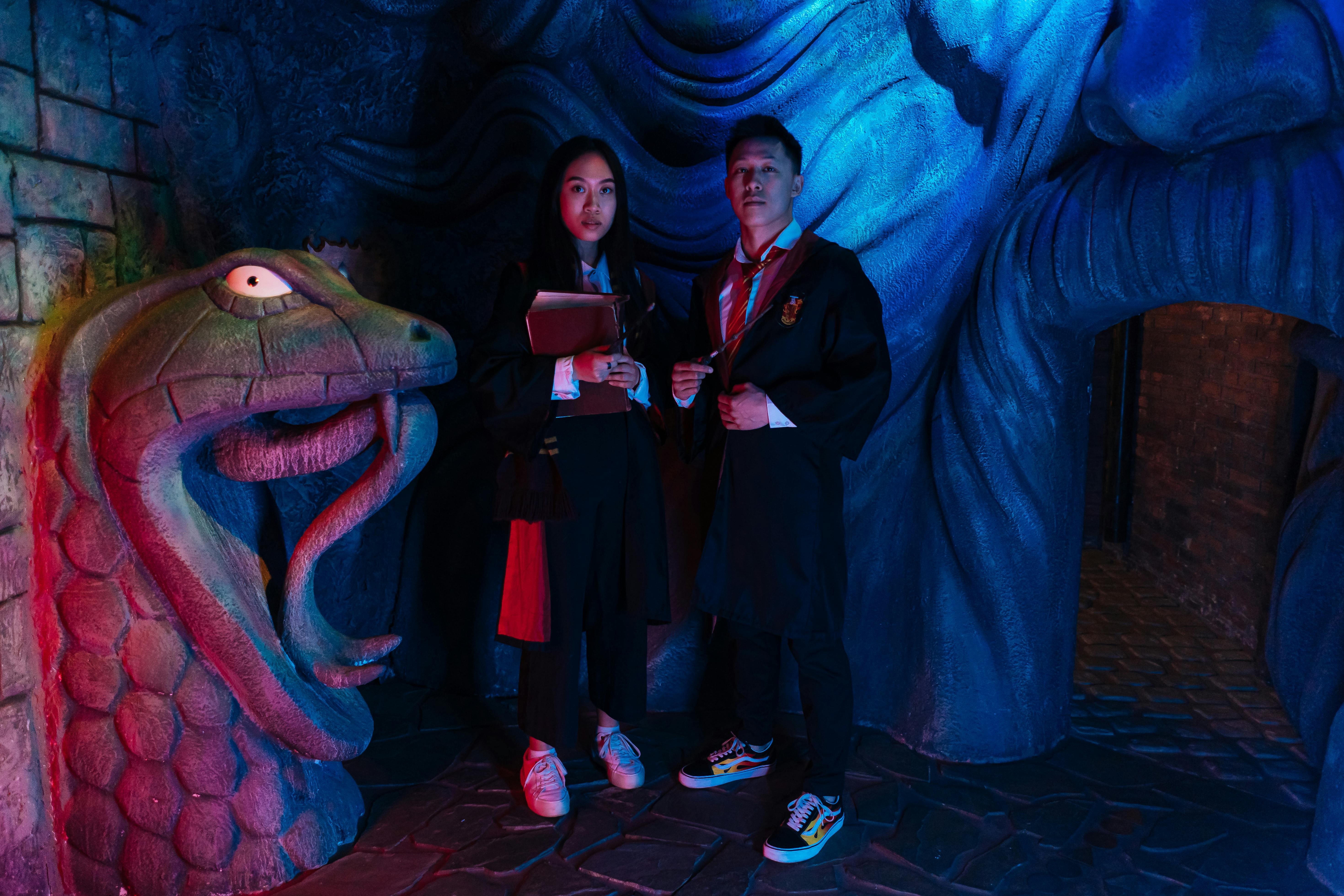 Free Two cosplayers in wizard attire pose in a mystical dungeon with serpentine décor and vibrant lighting. Stock Photo