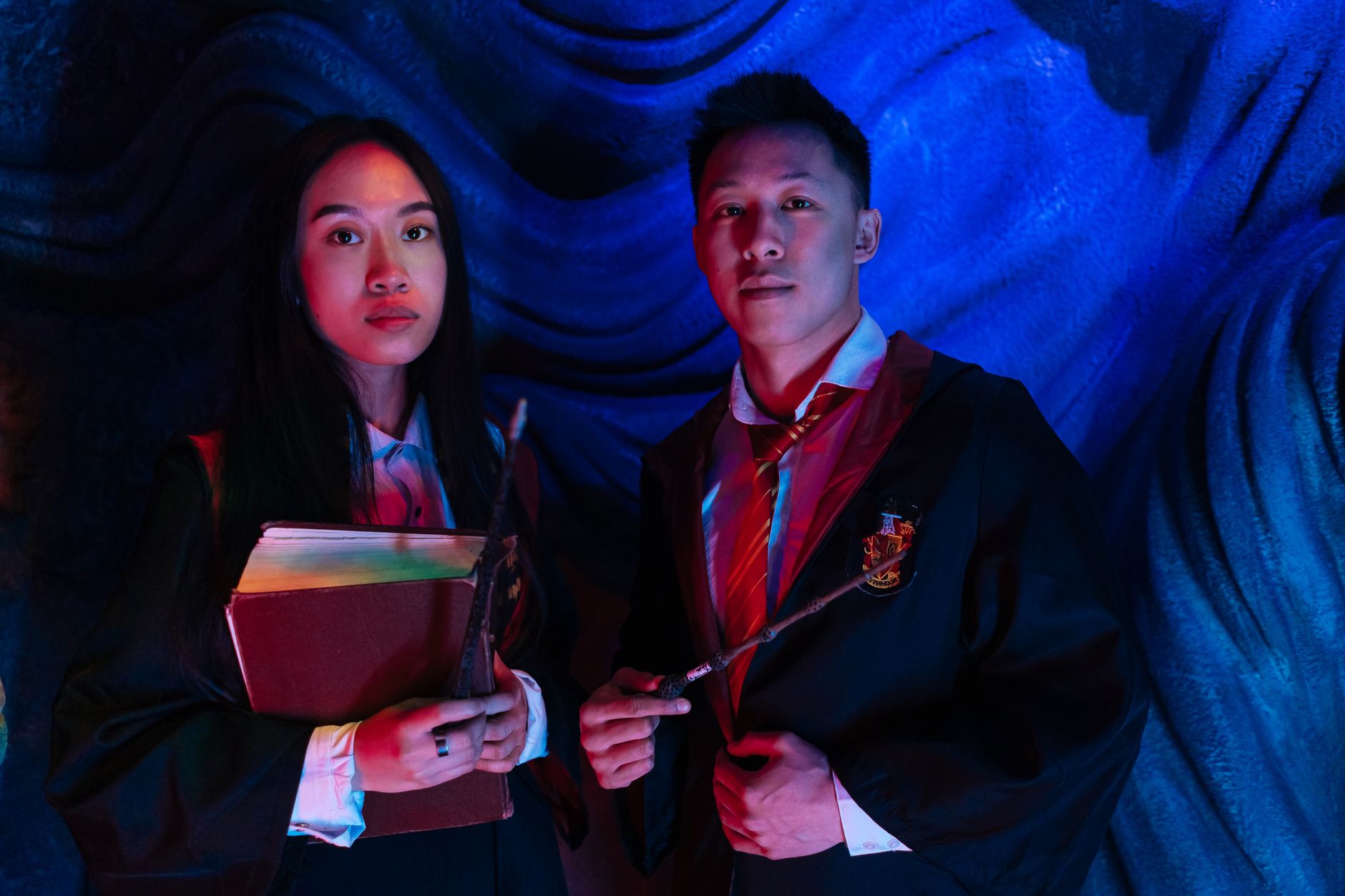 A couple dressed as wizards in a magic-themed studio with vibrant blue lighting.