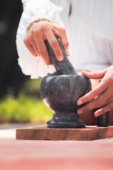 Hands grinding with a mortar and pestle on a wooden board outside in natural light.