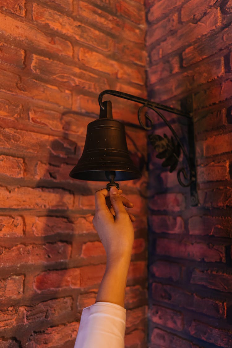 Close-Up Shot Of A Person Ringing A Bell Hanging From The Brick Wall