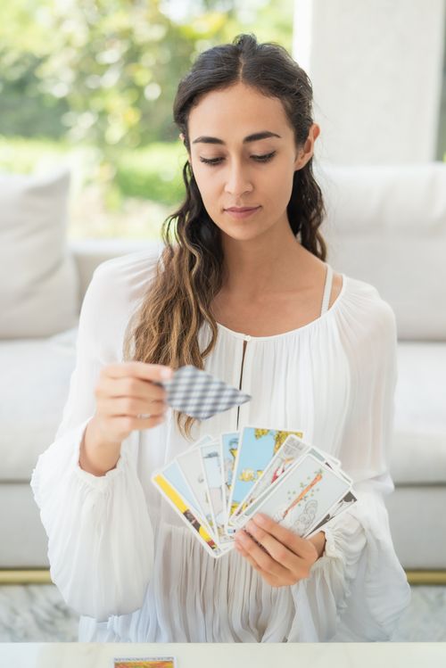 Free Female in white dress reading tarot cards indoors; a serene moment captured. Stock Photo