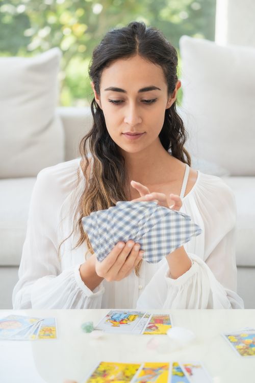Free Woman holding tarot cards in a serene, sunlit room, focusing on cartomancy. Stock Photo