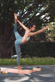 Woman performing a balance yoga pose on a mat in a peaceful outdoor setting.