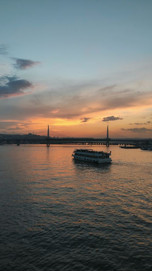 Free A serene sunset over Istanbul's Bosphorus with a boat gliding by the bridge, capturing a calm atmosphere. Stock Photo