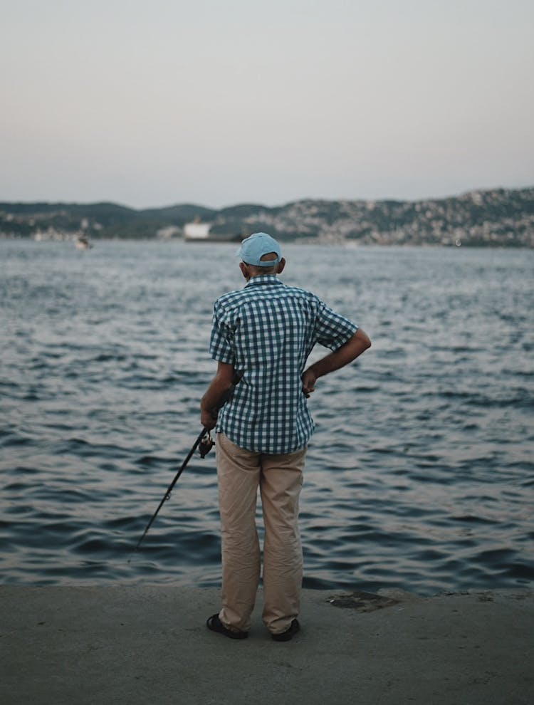 Back View Of An Elderly Man Fishing From A Pier 