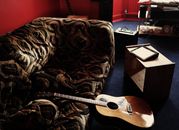 Brown Acoustic Guitar Leaning on Brown Velvet Couch