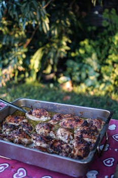 Close-up of seasoned chicken thighs on a tray in an outdoor setting, highlighting delicious food photography.