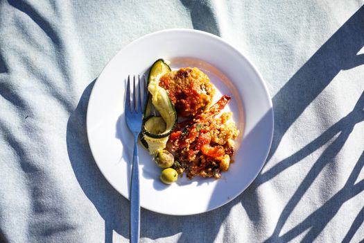 A vibrant meal of quinoa and vegetables served on a white plate with fork and shadows.