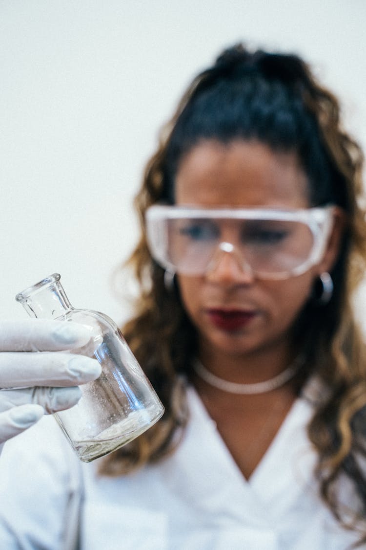 Woman In Protective Goggles Observing The Clear Glass Bottle 