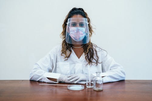 A Woman in White Lab Coat Looking while Wearing Face Mask and Face Shield
