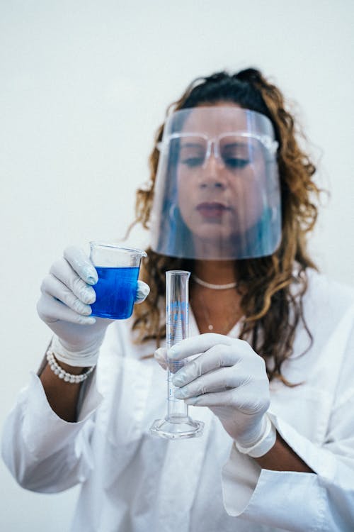Free Scientist Holding a Beaker With Blue Liquid and a Graduated Cylinder Stock Photo