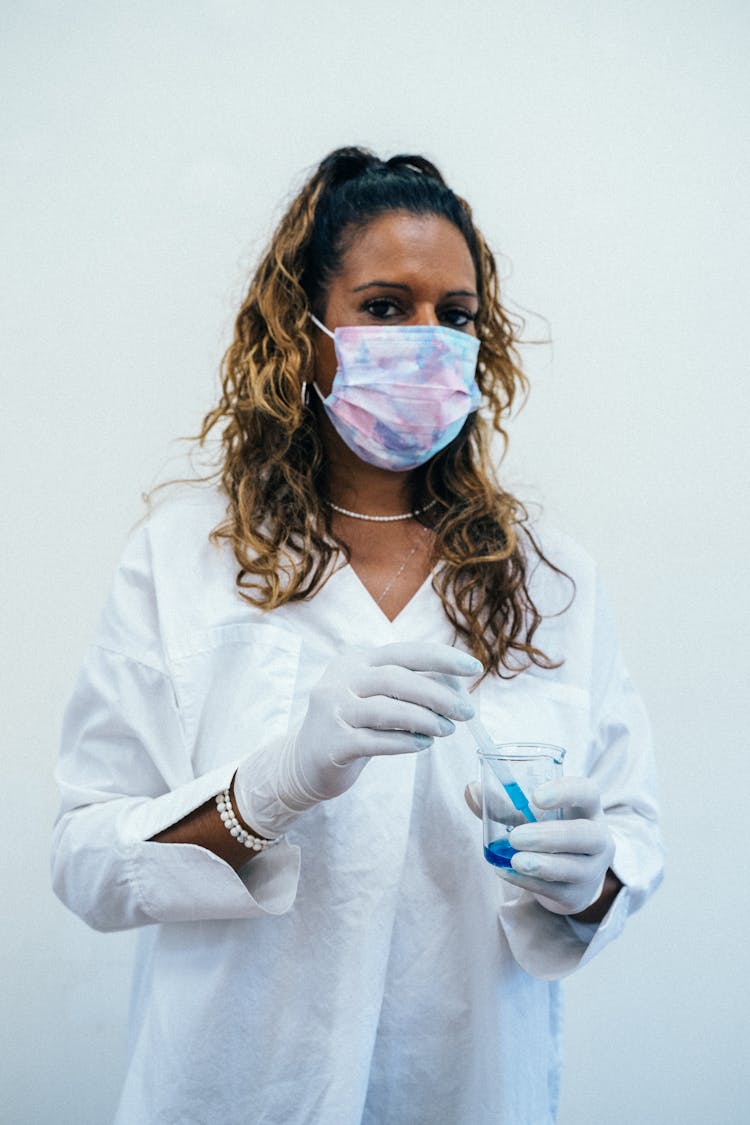 Curly Hair Woman With Face Mask Holding A Beaker And Dropper