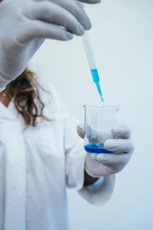 Person Holding a Dropper and Beaker With Blue Liquid 