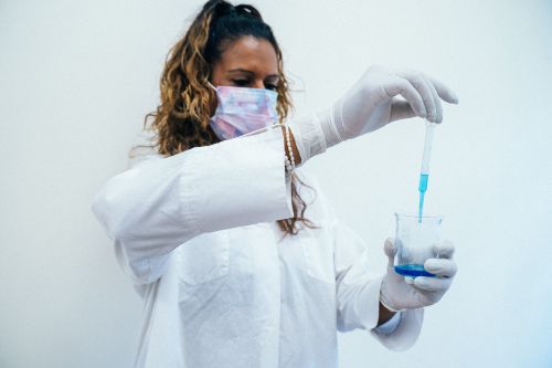 Free Female scientist using pipette in laboratory setting with beaker of blue liquid. Stock Photo