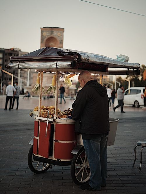 Free A street vendor stands with a food cart in Taksim Square, Istanbul, capturing local culture. Stock Photo