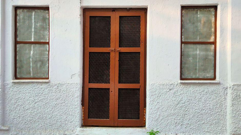 A rustic wooden door with iron mesh flanked by two windows on a white-textured wall. A rustic wooden door with iron mesh flanked by two windows on a white-textured wall.