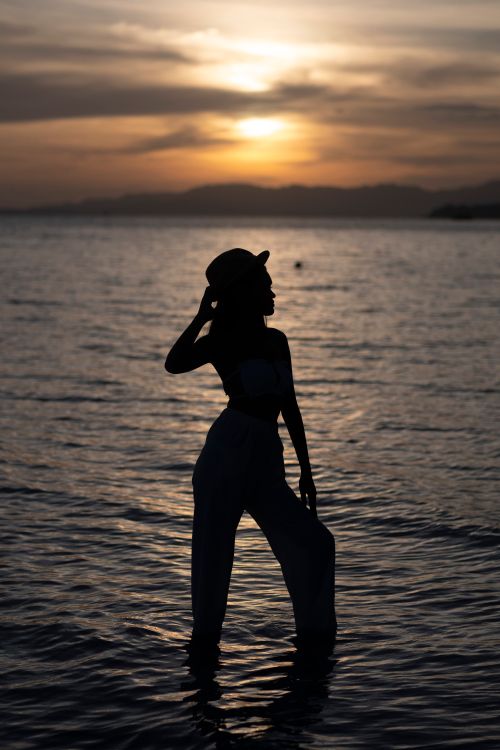 Free Silhouette of a woman standing on a beach during a stunning sunset in the Philippines. Stock Photo