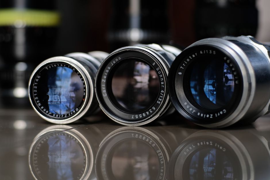 A detailed close-up of three Carl Zeiss Jena camera lenses reflecting light on a glass surface.