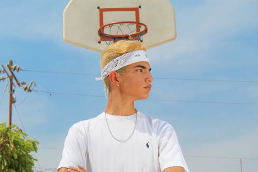 Confident young man with bandana standing near a basketball hoop on a sunny day.