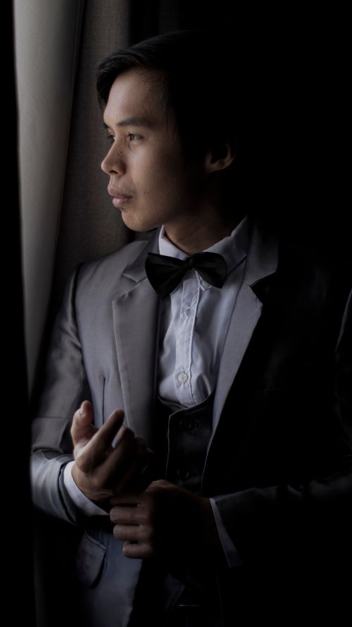 Free Elegant portrait of an Asian man in formal wear, gazing out a window with a contemplative expression. Stock Photo