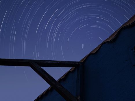 Stunning long-exposure photo of star trails swirling in the night sky above a rustic structure.