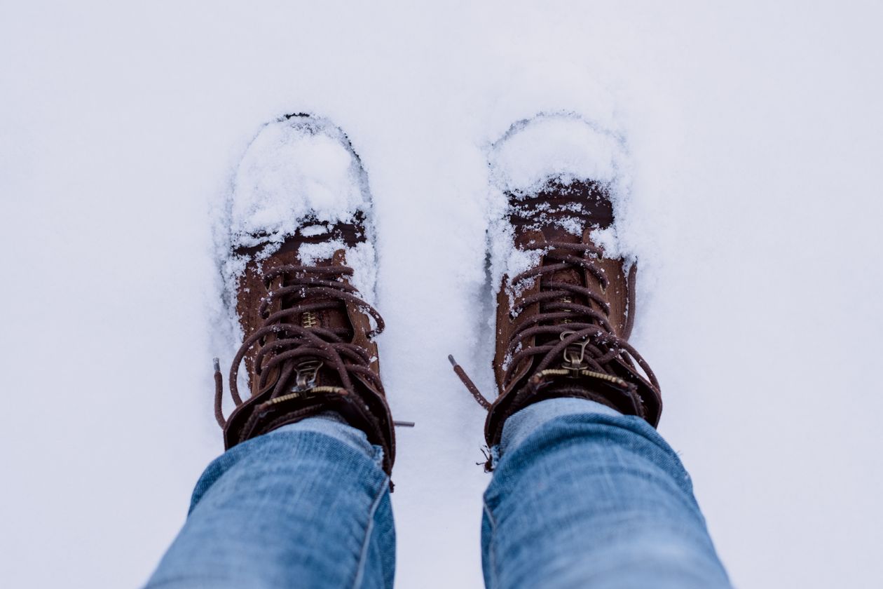 Overhead view of brown lace-up boots with jeans standing in snow