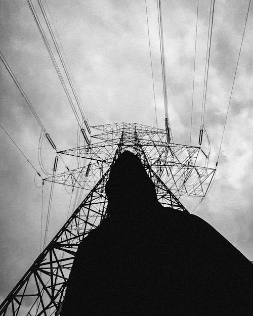 Silhouette of Person Standing Near a Power Line