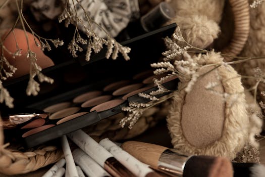 A flat lay of a makeup palette surrounded by brushes and dried branches, creating a cozy and artistic ambiance.