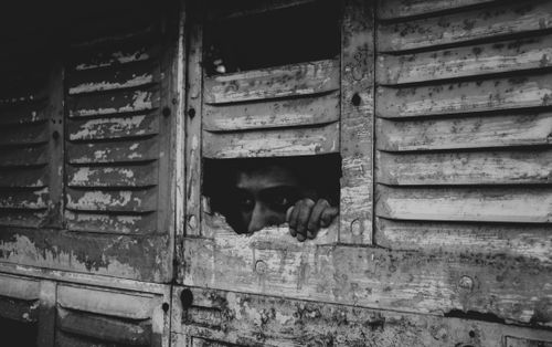 Free A monochromatic image of a person peering through a broken window, evoking a sense of mystery and solitude. Stock Photo