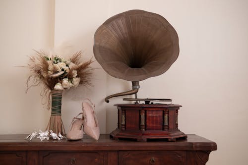 Antique Gramophone Beside a Pair of High Heels and Flower Vase on Wooden Chest Drawer