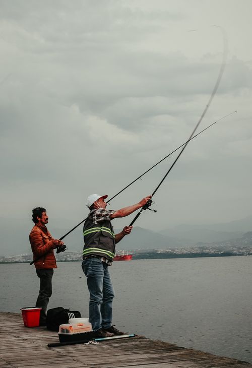 Free Two men fishing on a dock in Kocaeli, Türkiye, with fishing rods and equipment on a cloudy day. Stock Photo